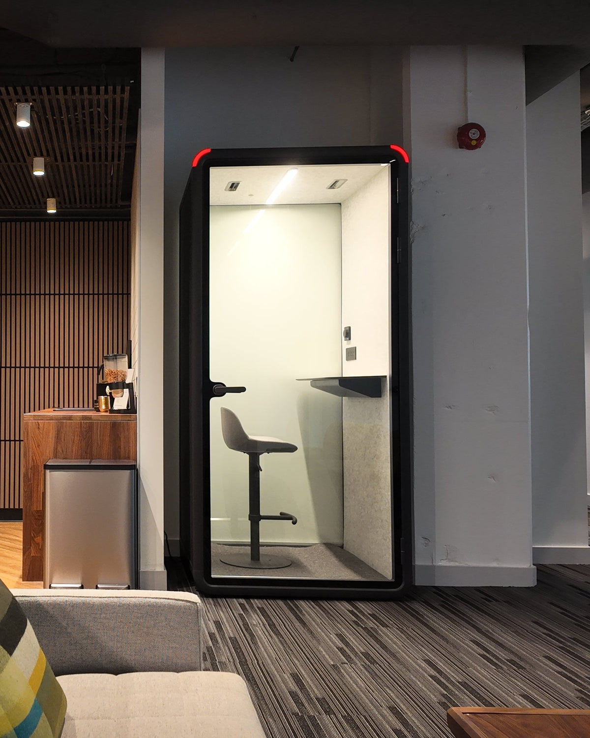 Single Work Booth in a lounge area beside the seating, seen from across the room ::real