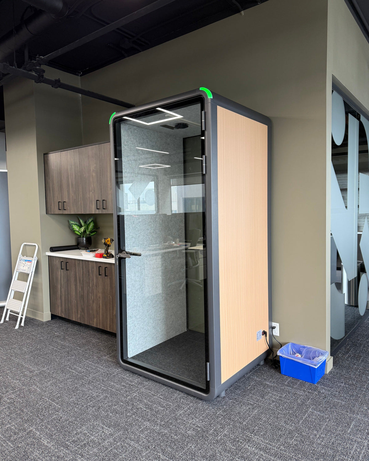 Single Work Booth with a wood side panel, parked beside an office kitchen. It reads as furniture, not equipment ::real