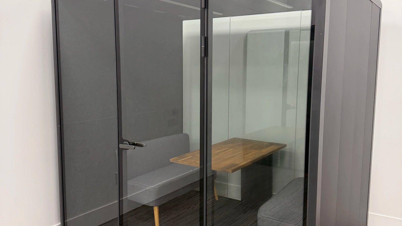 A Collaborative Booth installed in the corner of an office, bench seating and shared table visible through the glass
