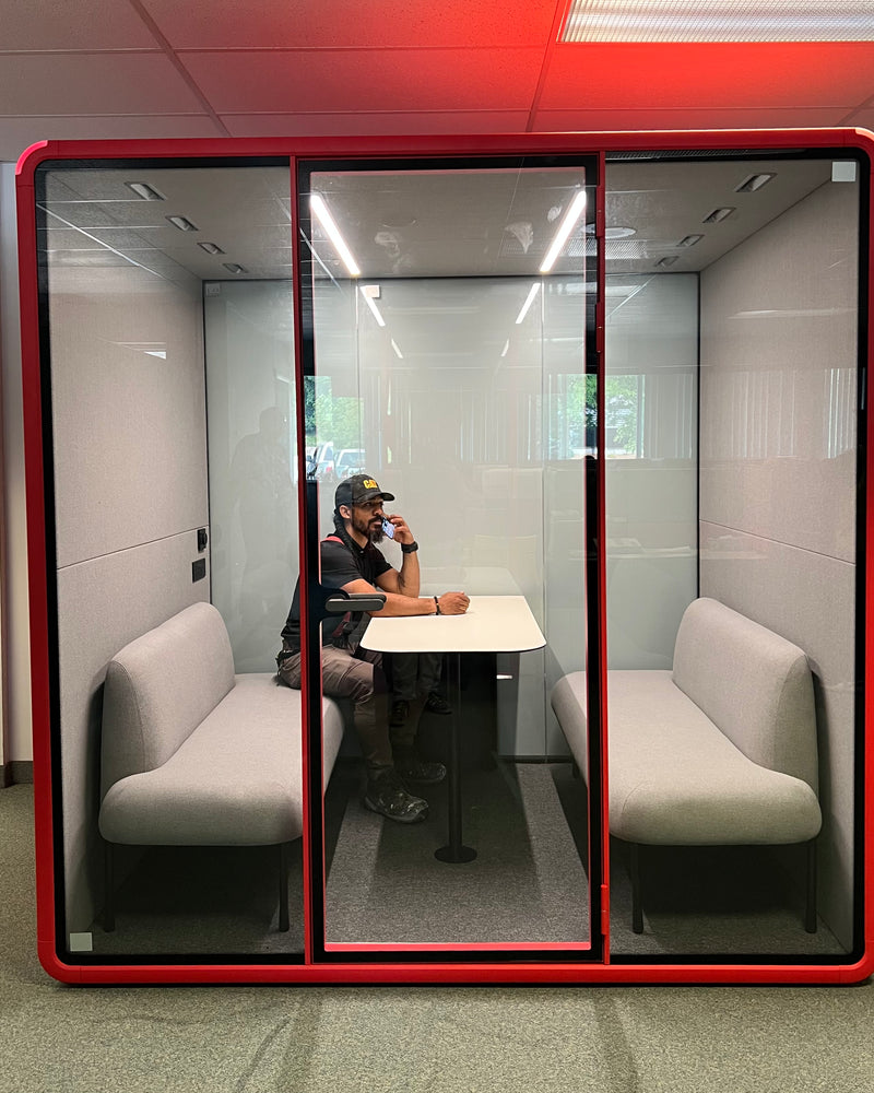 A person taking a call inside a Quiet Cabins Collaborative Booth on an operations office floor