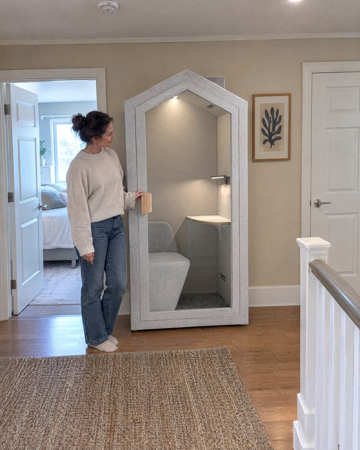 A woman standing beside the Home Pod on an upstairs landing, next to a bedroom door for scale. Illustration.
