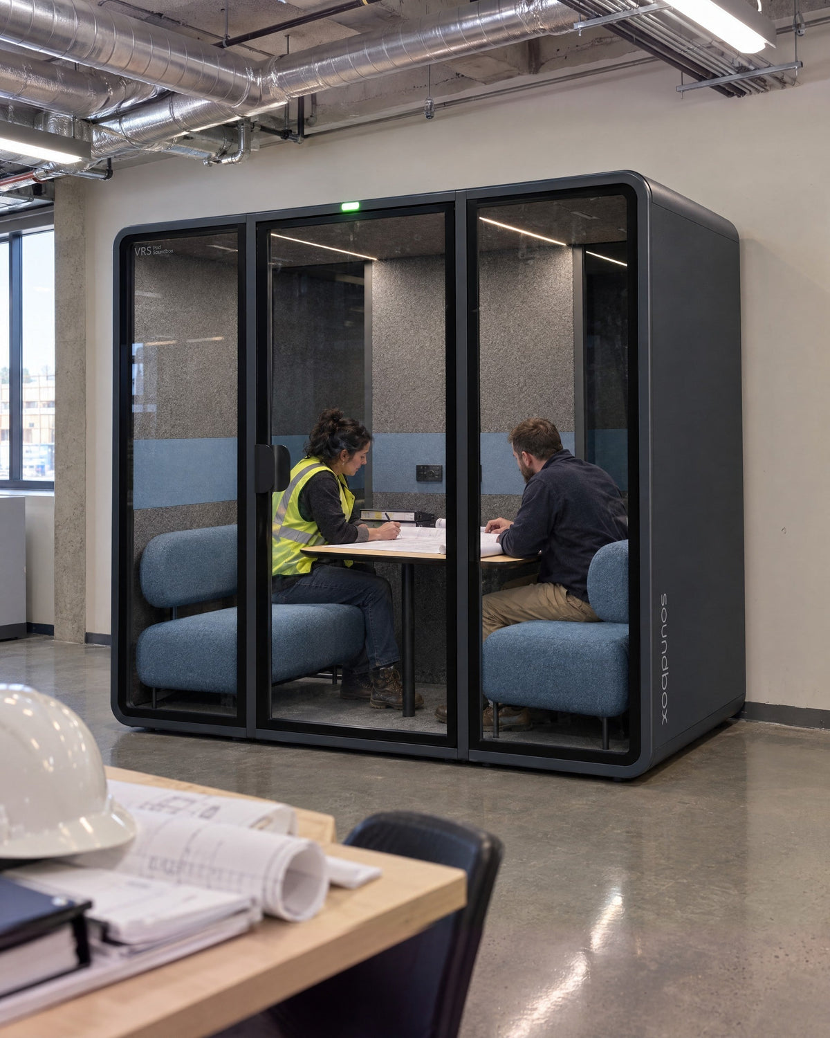 SoundBox VRS Double in a construction site office, two people reviewing drawings inside, hard hat and plans in the foreground. Illustration.