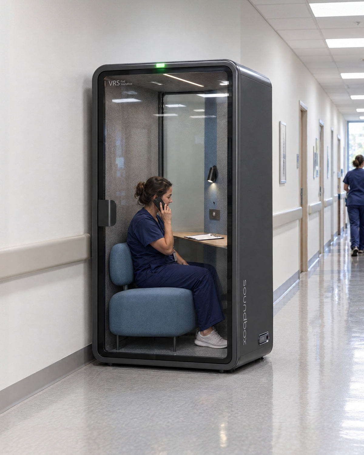 SoundBox VRS Single Comfort in a hospital administration corridor, a nurse inside on a phone call. Illustration.
