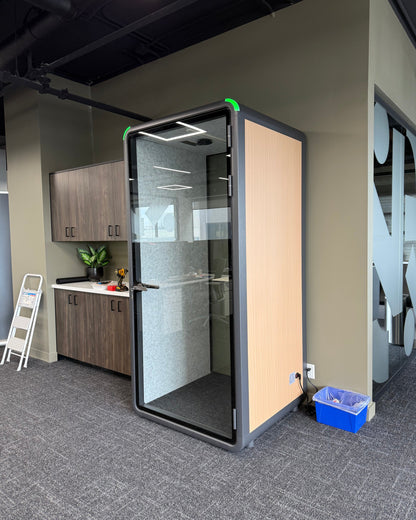 Single Work Booth with a wood side panel, parked beside an office kitchen. It reads as furniture, not equipment ::real