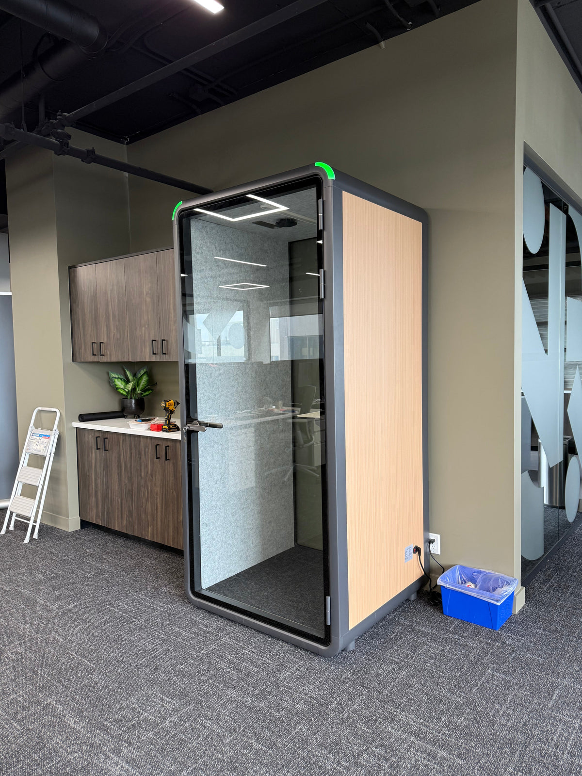 Single Work Booth with a wood side panel, parked beside an office kitchen. It reads as furniture, not equipment ::real