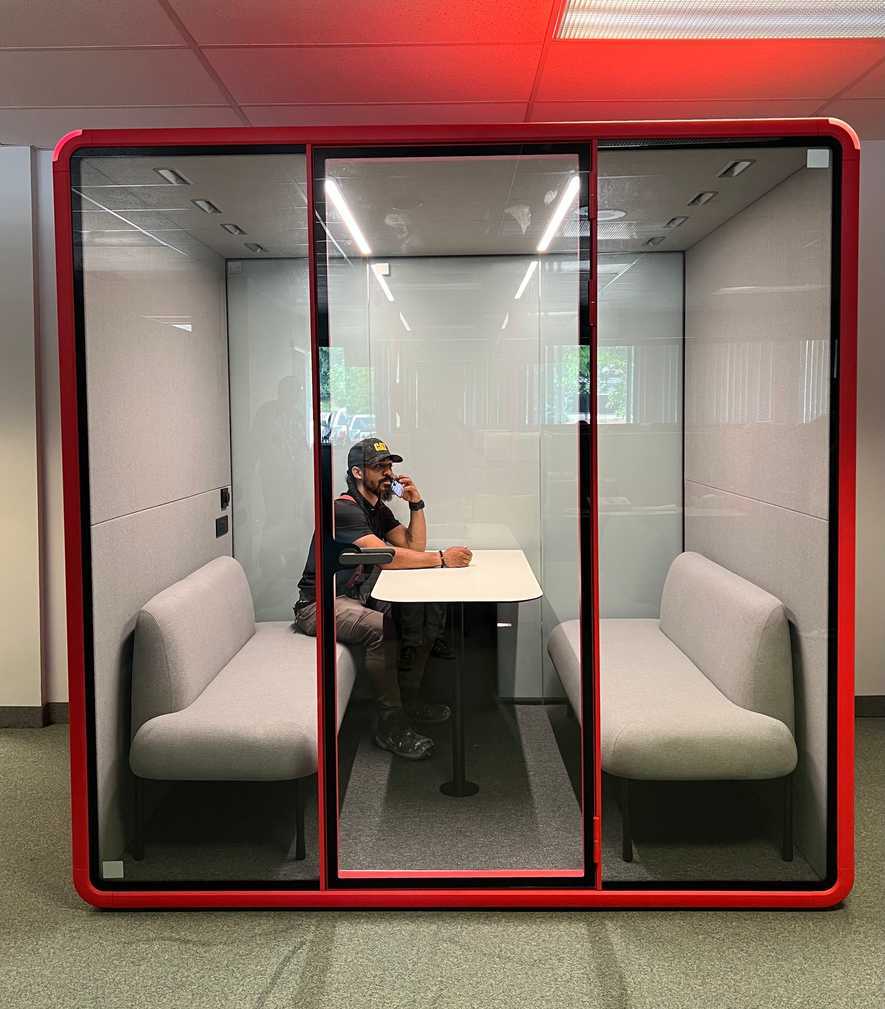 A person taking a call inside a Quiet Cabins Collaborative Booth on an operations office floor