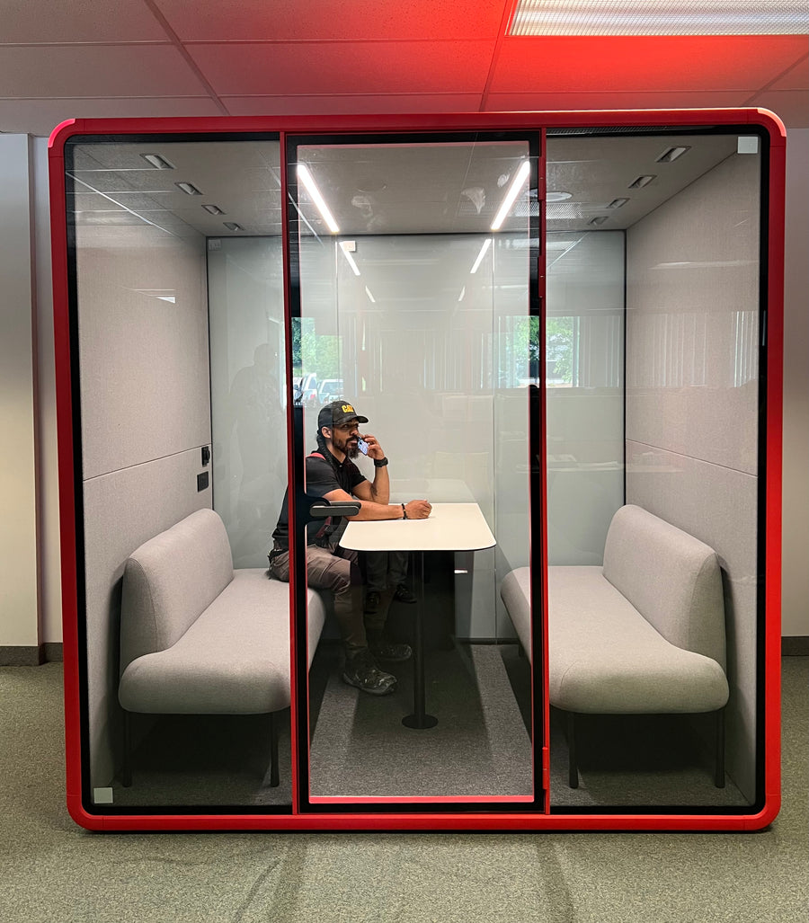 A man on a phone call inside the finished red Collaborative booth with the door shut
