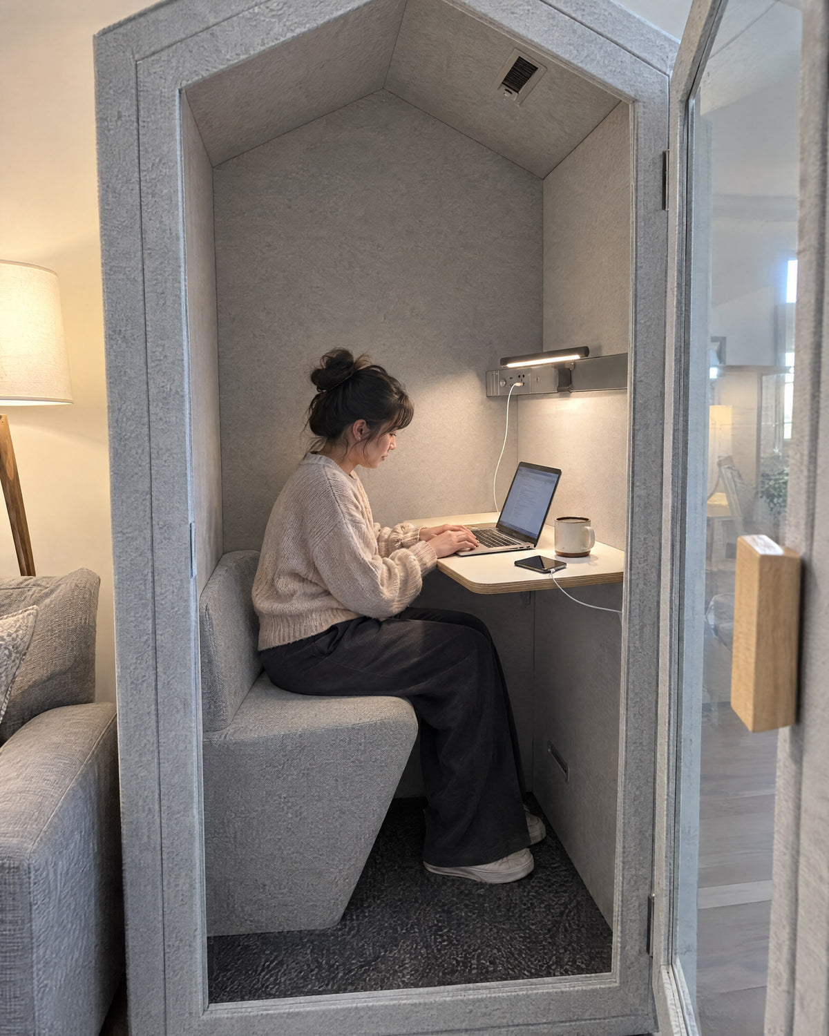 Inside the Home Pod with the door open: curved seat, wall desk with a laptop, lamp bar and a phone charging from the power panel. Illustration.