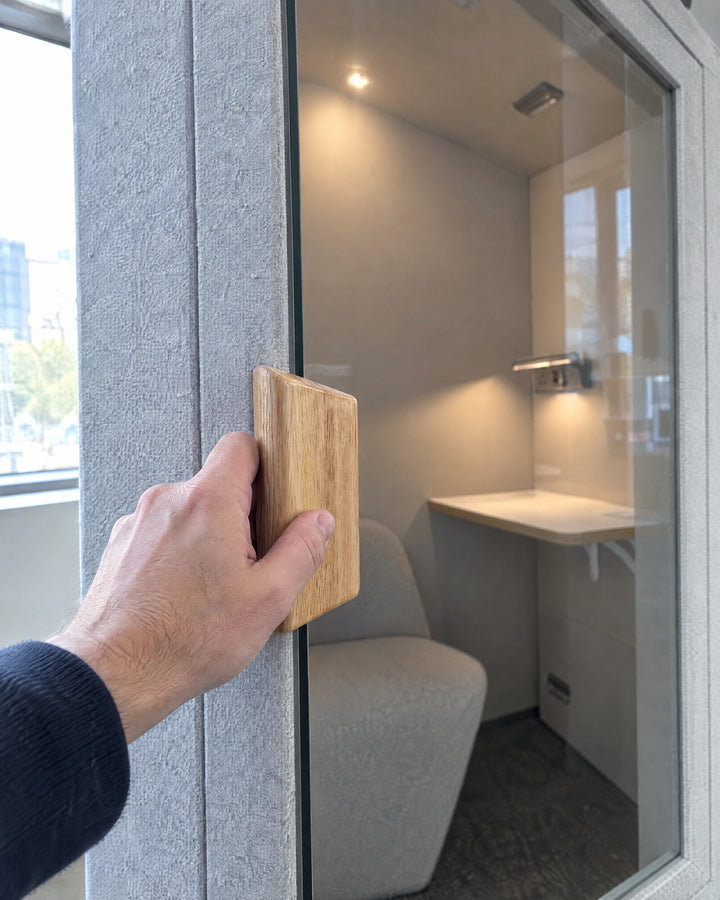 A hand opening the Home Pod door by its oak block handle, felt frame and lit interior behind. Illustration.