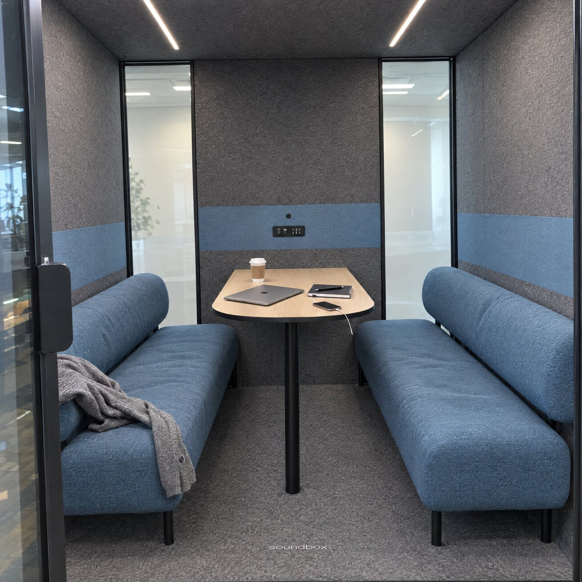 Inside the Soundbox VRS Collaborative between meetings: two dusty blue sofas facing each other, an oak table from the back wall, glass at both ends of the back wall