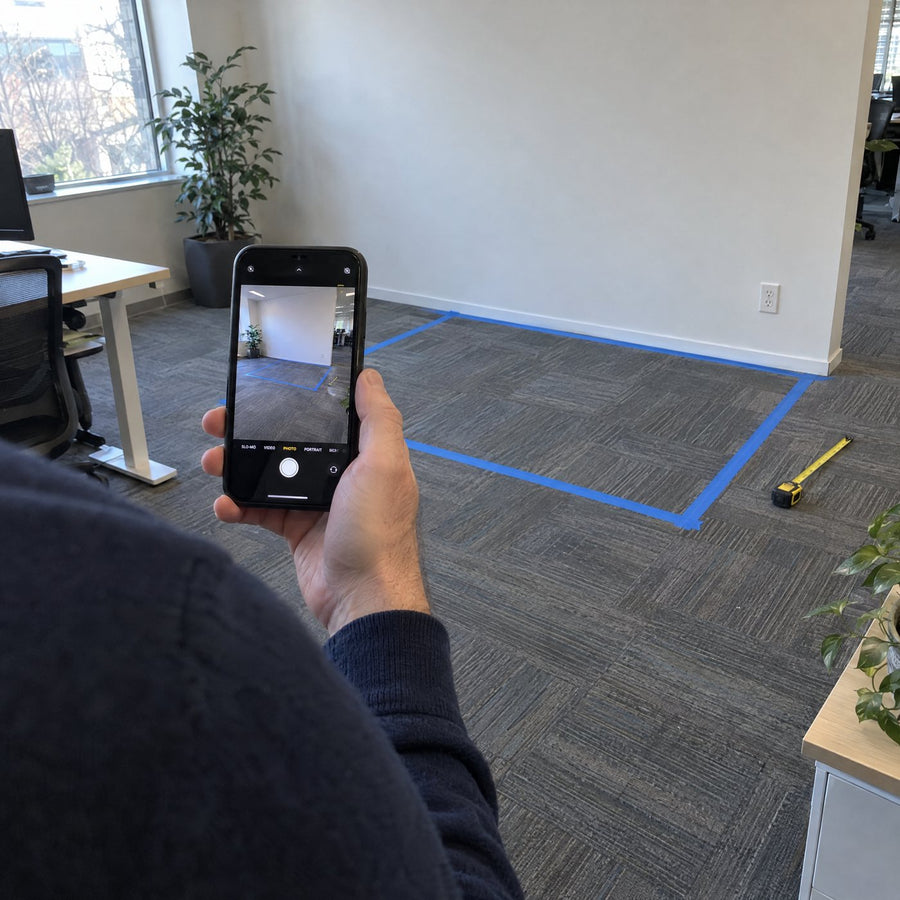 Someone photographing a taped-out pod footprint on an office floor with a phone