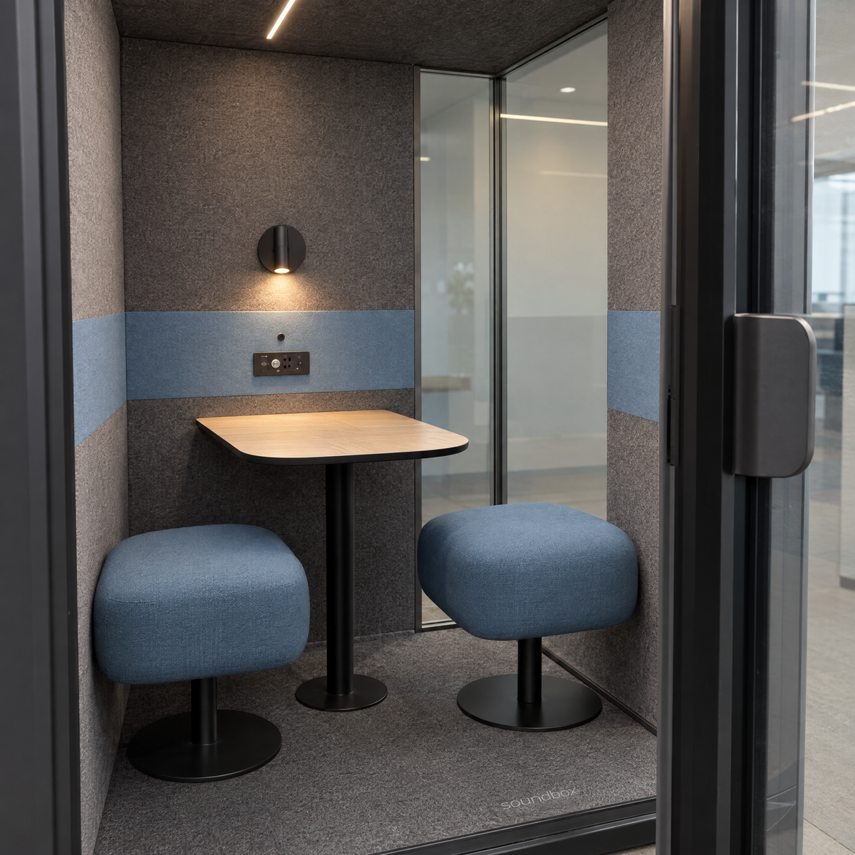 Inside the SoundBox VRS Comfort through the open door: two backless dusty blue seats and a small oak table, wall lamp and control panel on the felt back wall, glass on the right half of the back wall. Illustration.