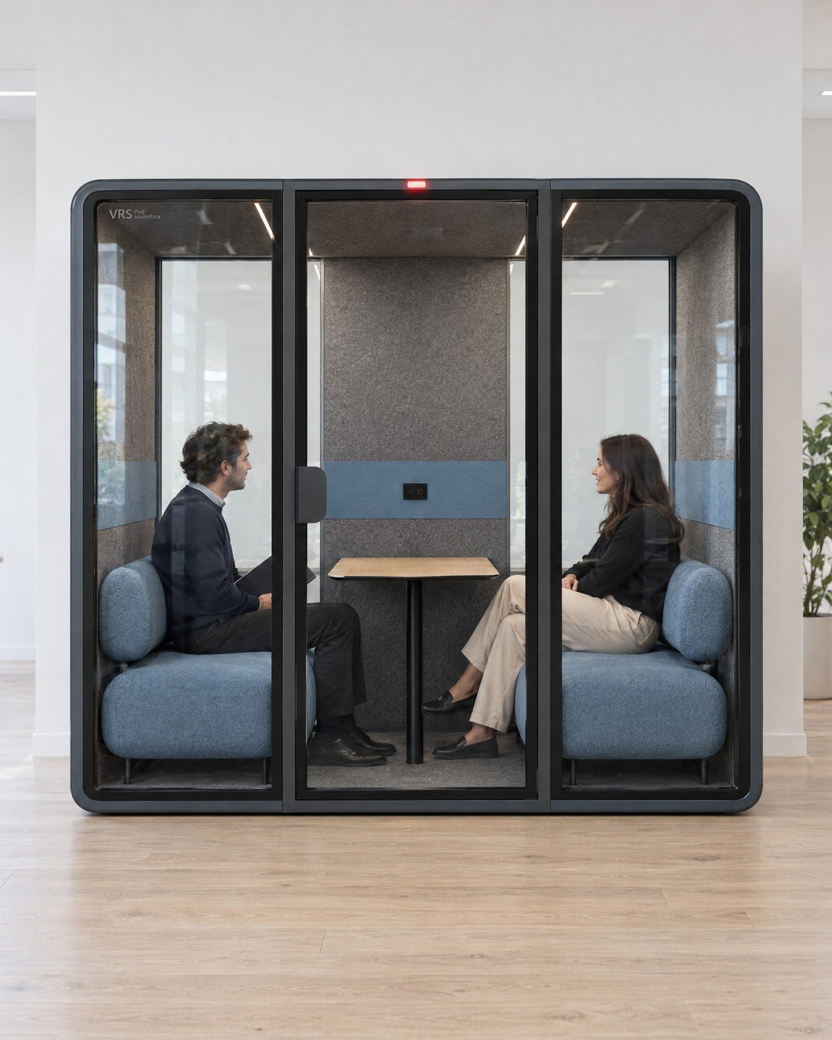 Two people in a private conversation inside a SoundBox VRS Double in an open office, red occupied light on. Illustration.
