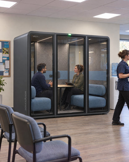 SoundBox VRS Double in a community clinic staff area seen from the waiting chairs, two people in a private conversation inside. Illustration.