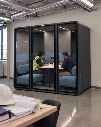 SoundBox VRS Double in a construction site office, two people reviewing drawings inside, hard hat and plans in the foreground. Illustration.