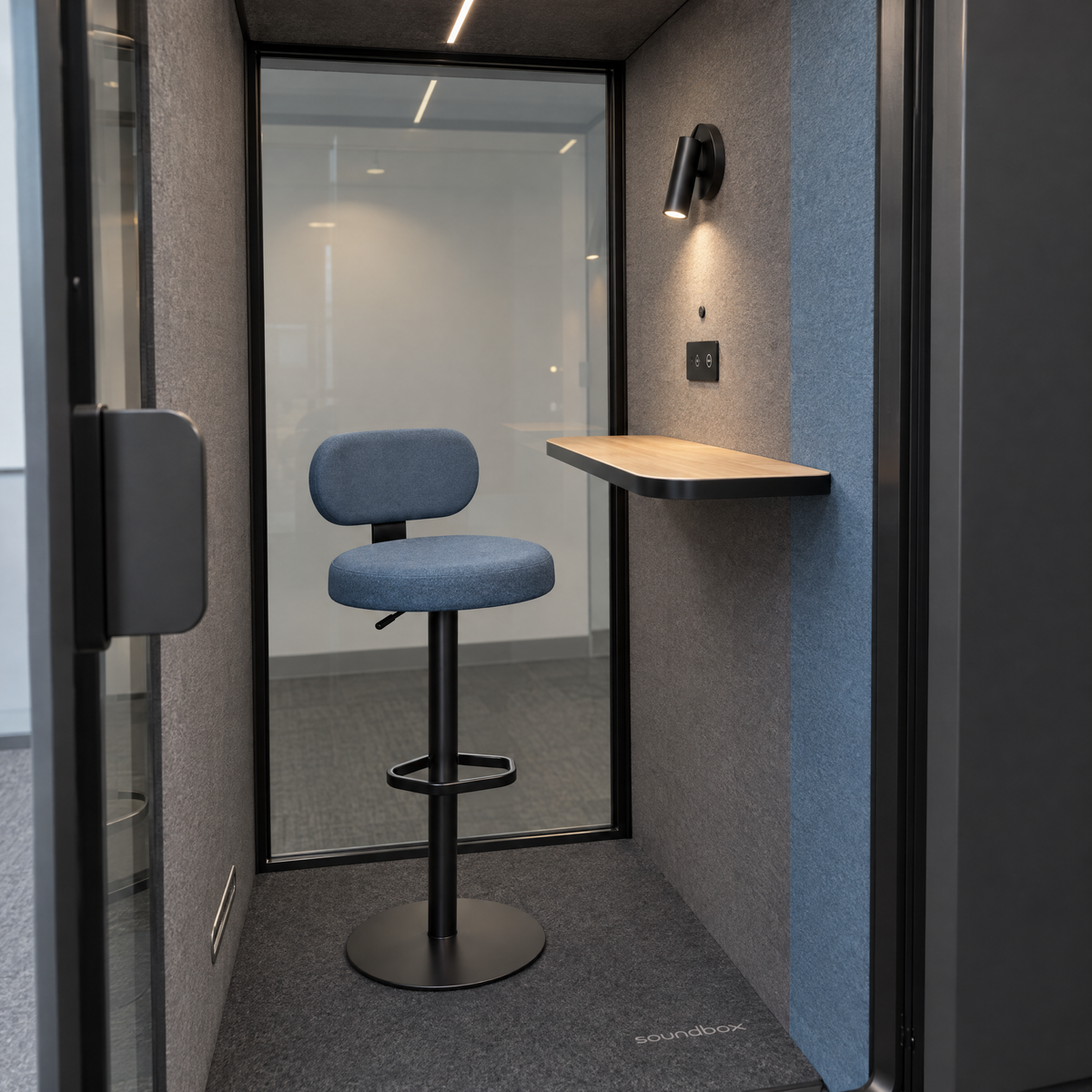 Inside the SoundBox VRS Single through the open door: dusty blue bar stool, oak desk shelf, spot lamp and control panel, full-height glass back wall. Illustration.