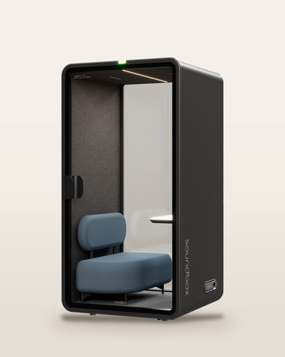 SoundBox VRS Single Comfort pod: graphite shell, full-height glass door, dusty blue lounge armchair and oak desk shelf inside