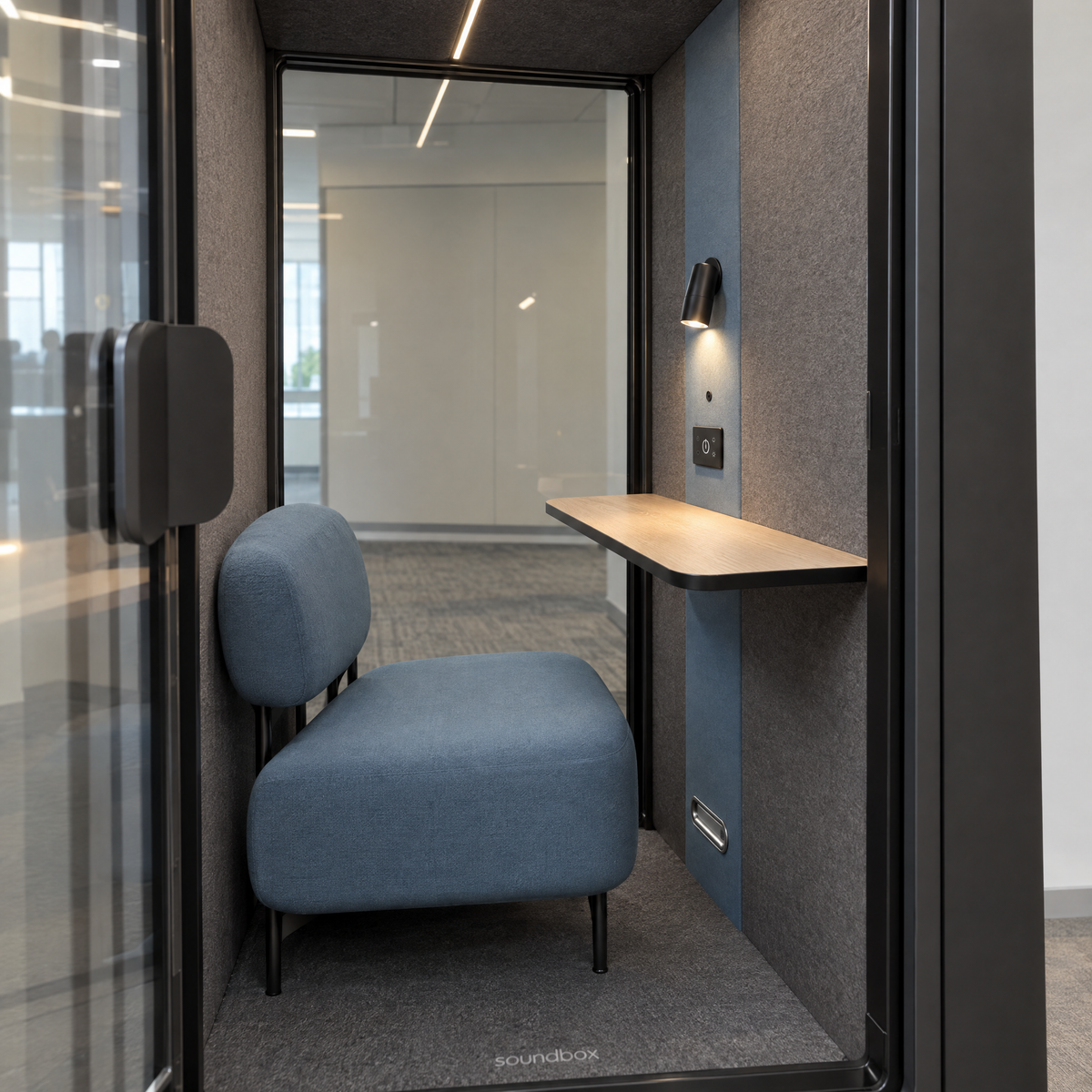 Inside the SoundBox VRS Single Comfort through the open door: dusty blue lounge armchair, oak desk shelf, spot lamp and control panel, full-height glass back wall. Illustration.