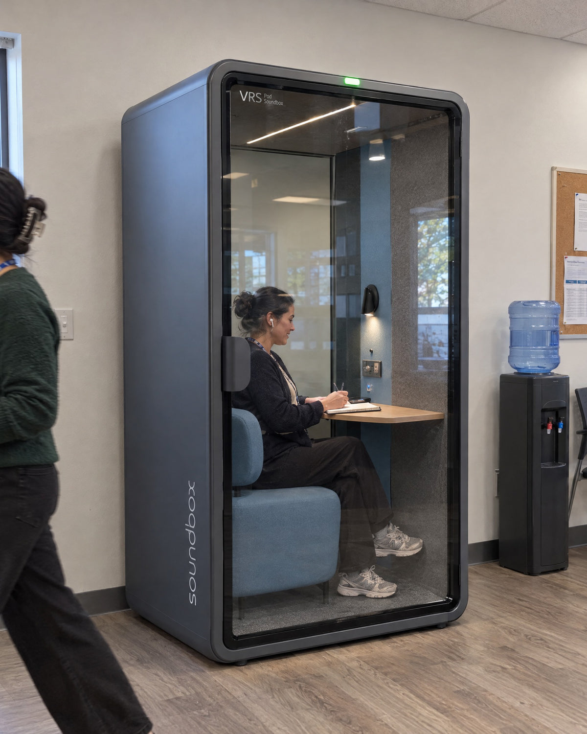 SoundBox VRS Single Comfort in a community clinic staff area, a clinician inside on a telehealth call. Illustration.