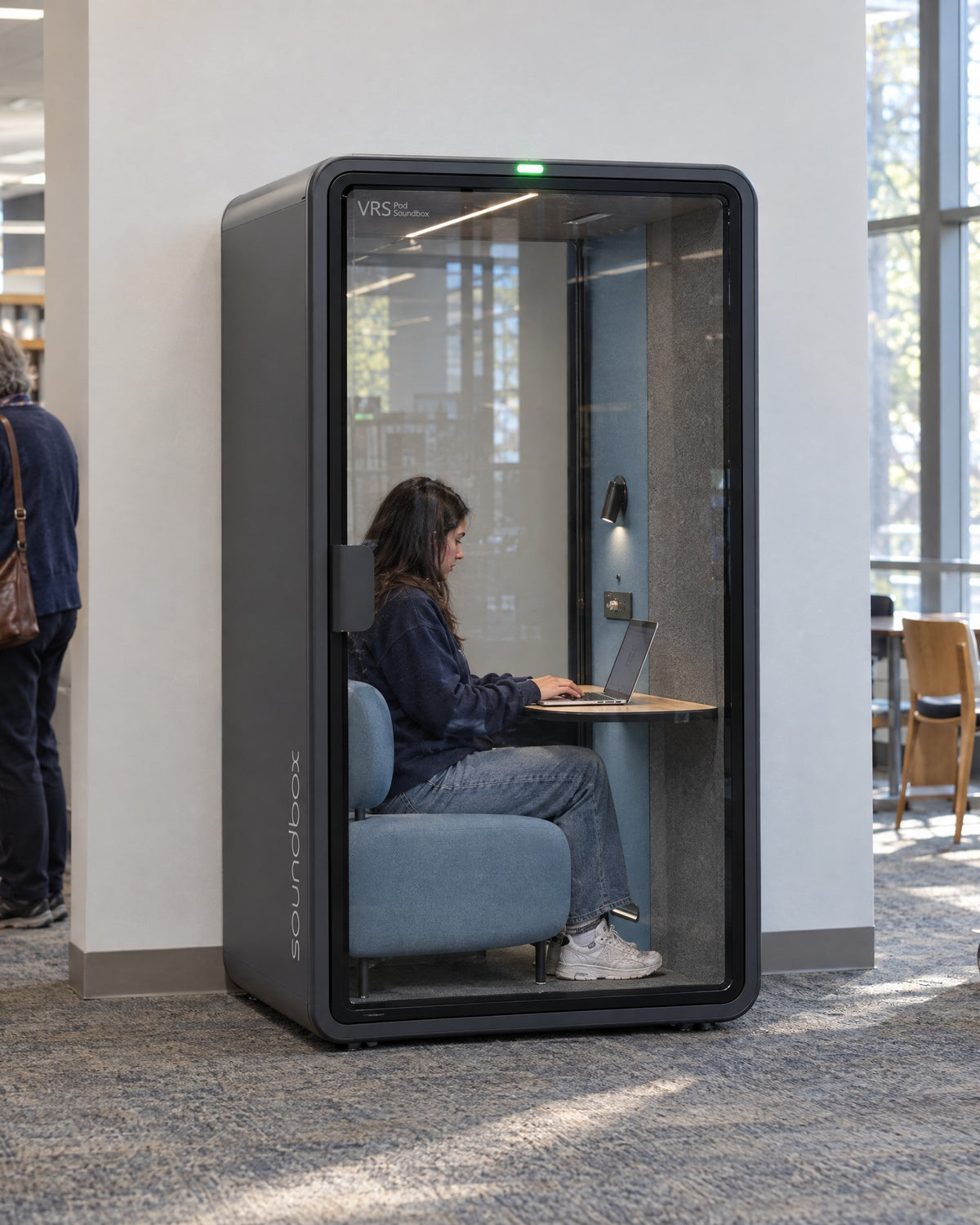 SoundBox VRS Single Comfort in a public library, a student inside working on a laptop. Illustration.
